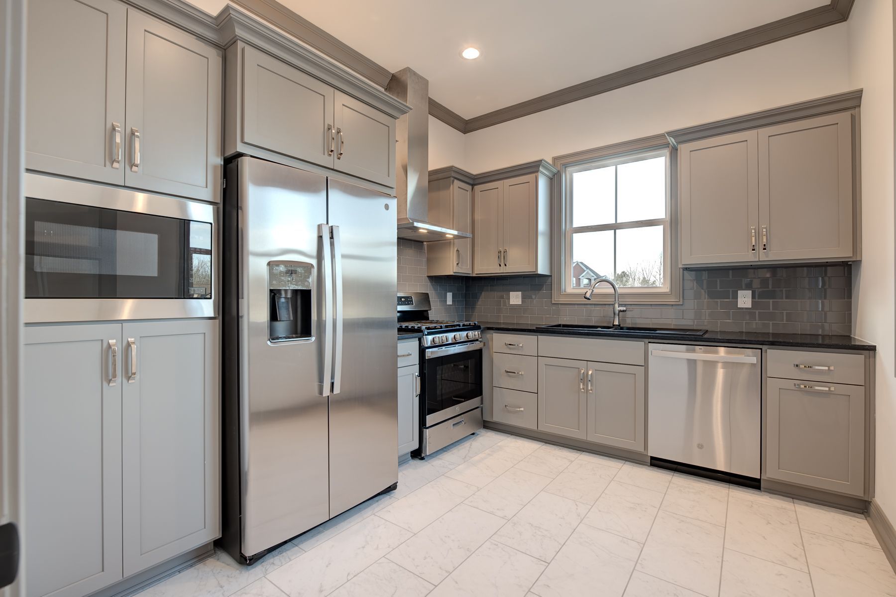 Gray modern kitchen with stainless steel appliances, cabinets, and a window.