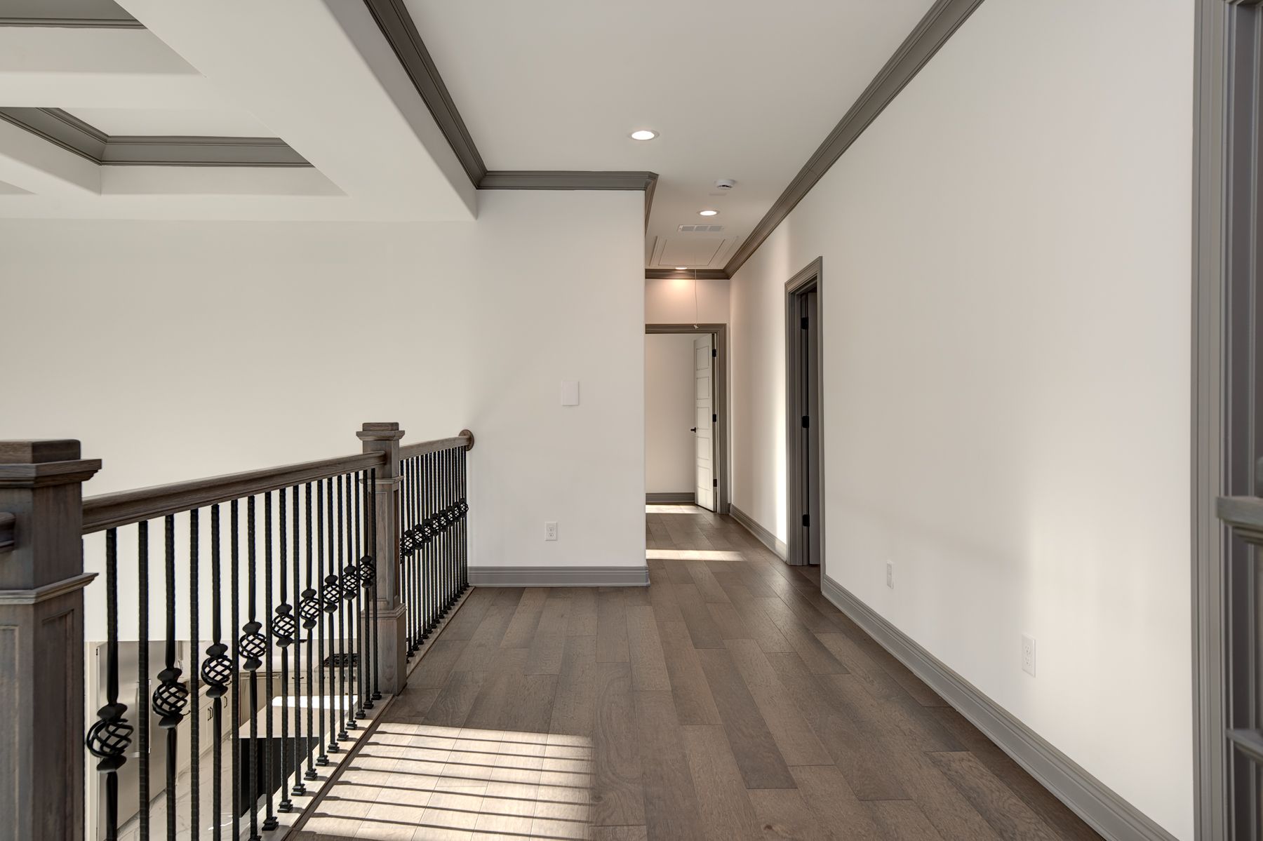 Hallway with wood floors, white walls, and dark gray trim and railing.