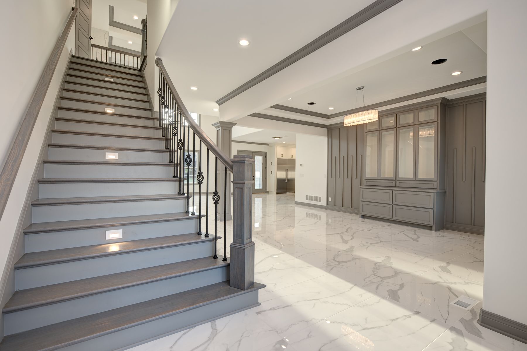 Gray staircase with black railing leads to a hallway with marble tile floor and built-in gray cabinets.
