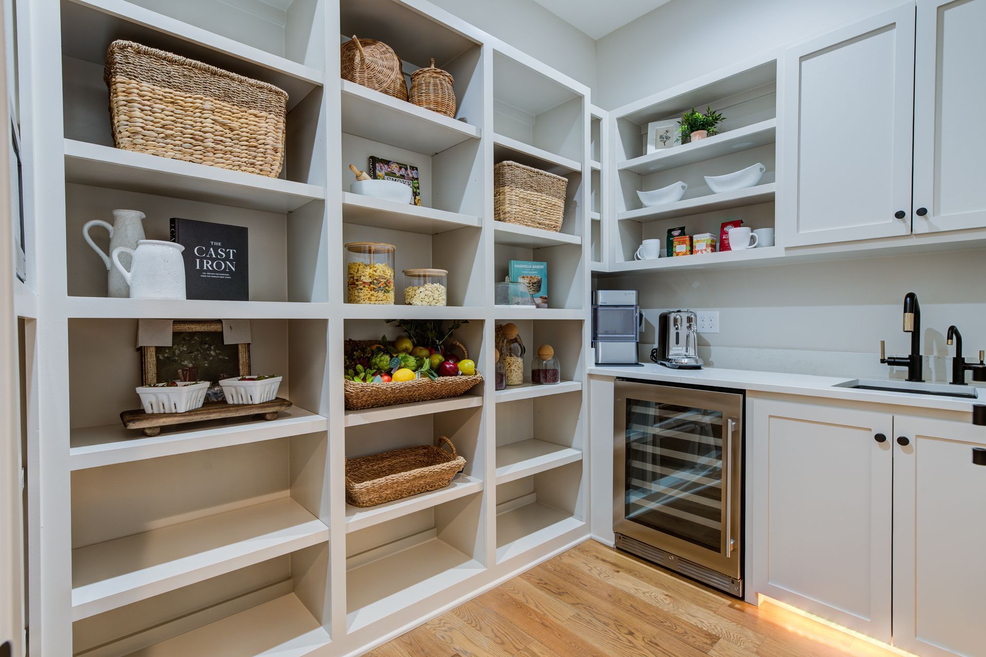 White pantry with built-in shelves, baskets, a wine fridge, and a sink.