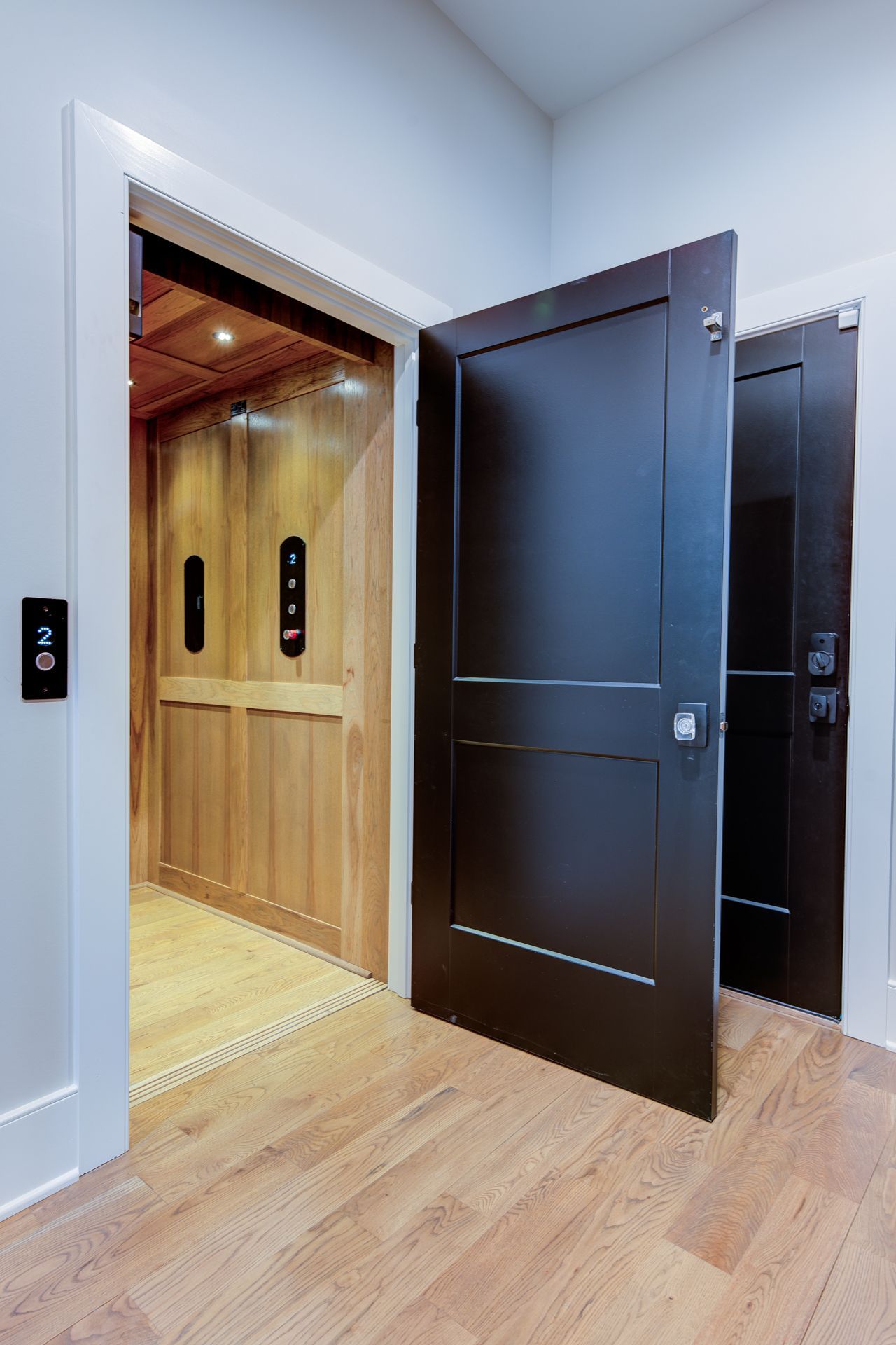 Open door reveals a home elevator with wood paneling. Another door is partially visible.