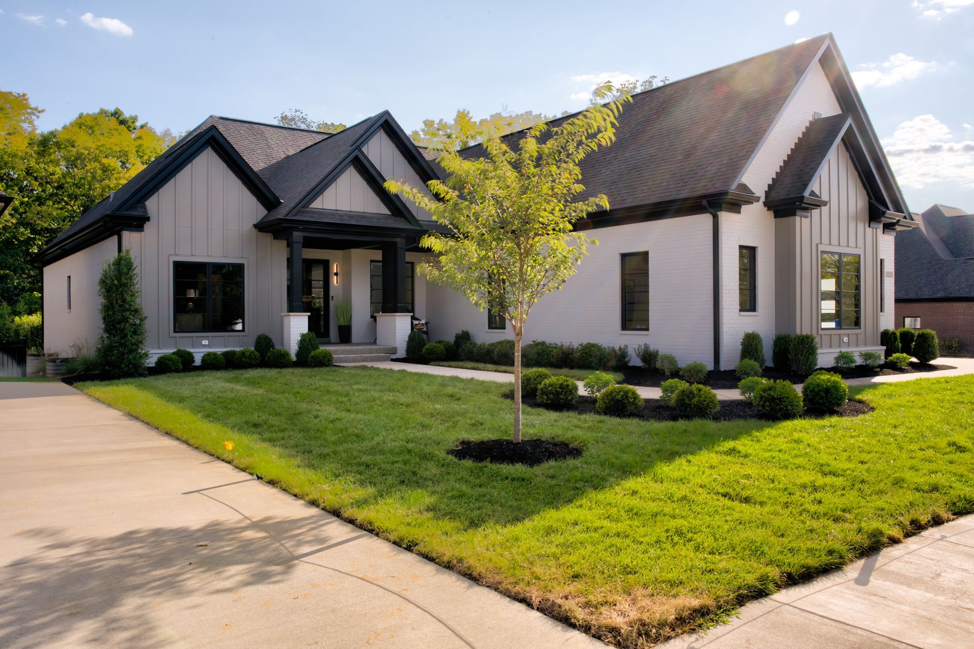 Modern white house with dark trim, green lawn, and driveway on a sunny day