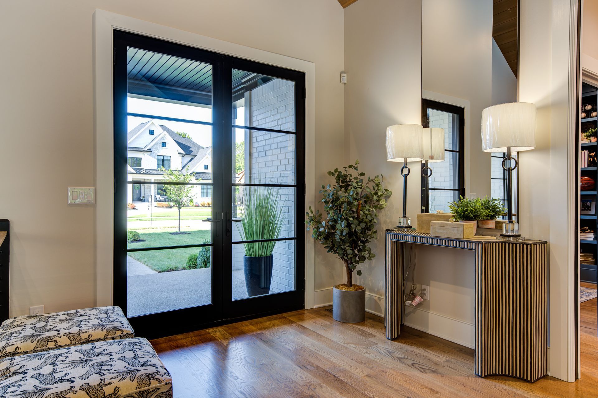 Entryway with black-framed glass doors, wooden floor, console table with lamps, and a bench.