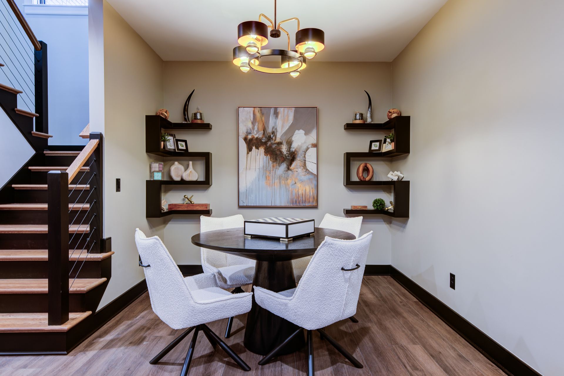 Dining area with round table and four chairs, under a chandelier, with floating shelves and a staircase.