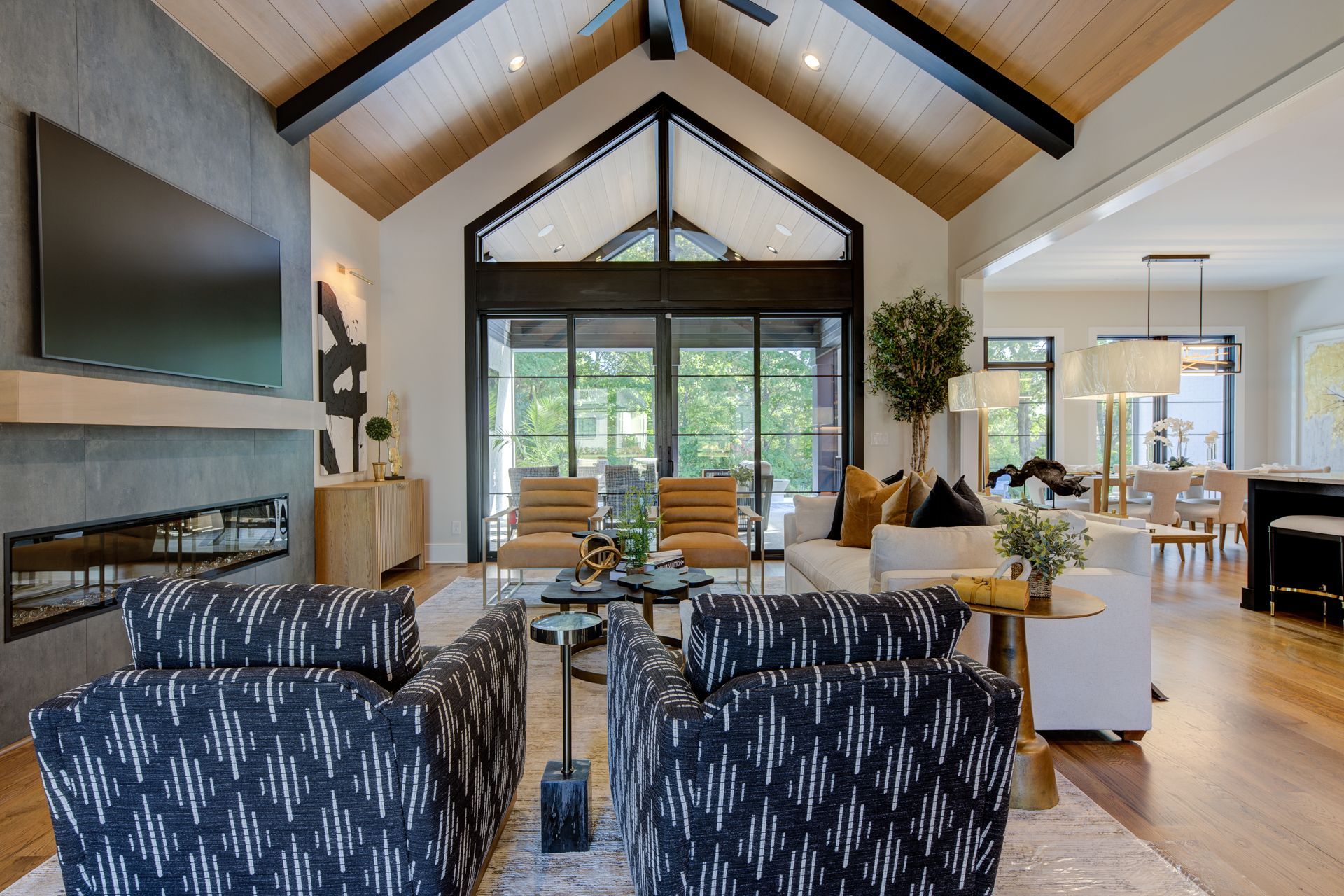 Living room with high ceilings, fireplace, and patterned armchairs. Large windows offer a view outside.