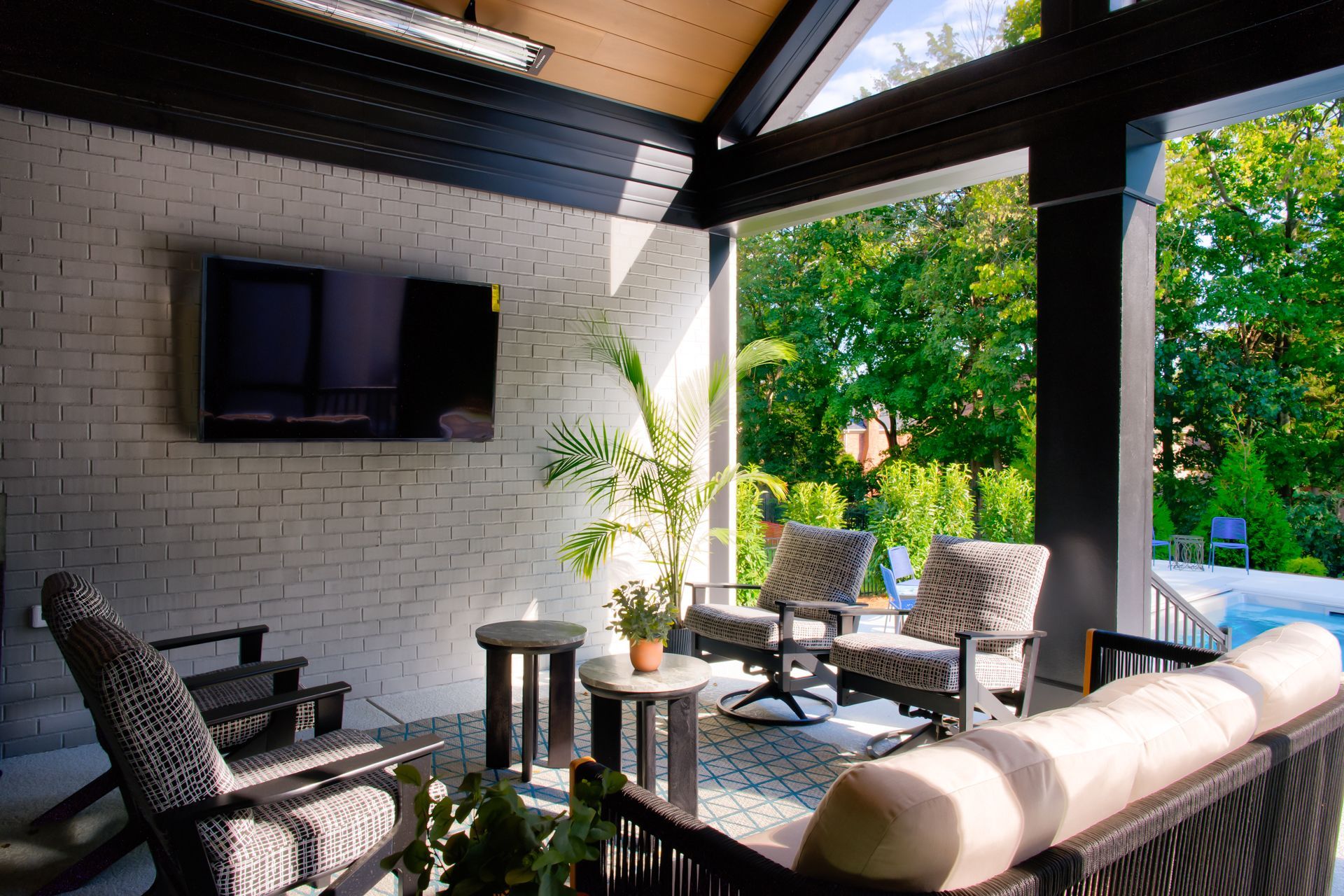 Outdoor patio with furniture, a television, and a brick wall. View of trees in the distance.