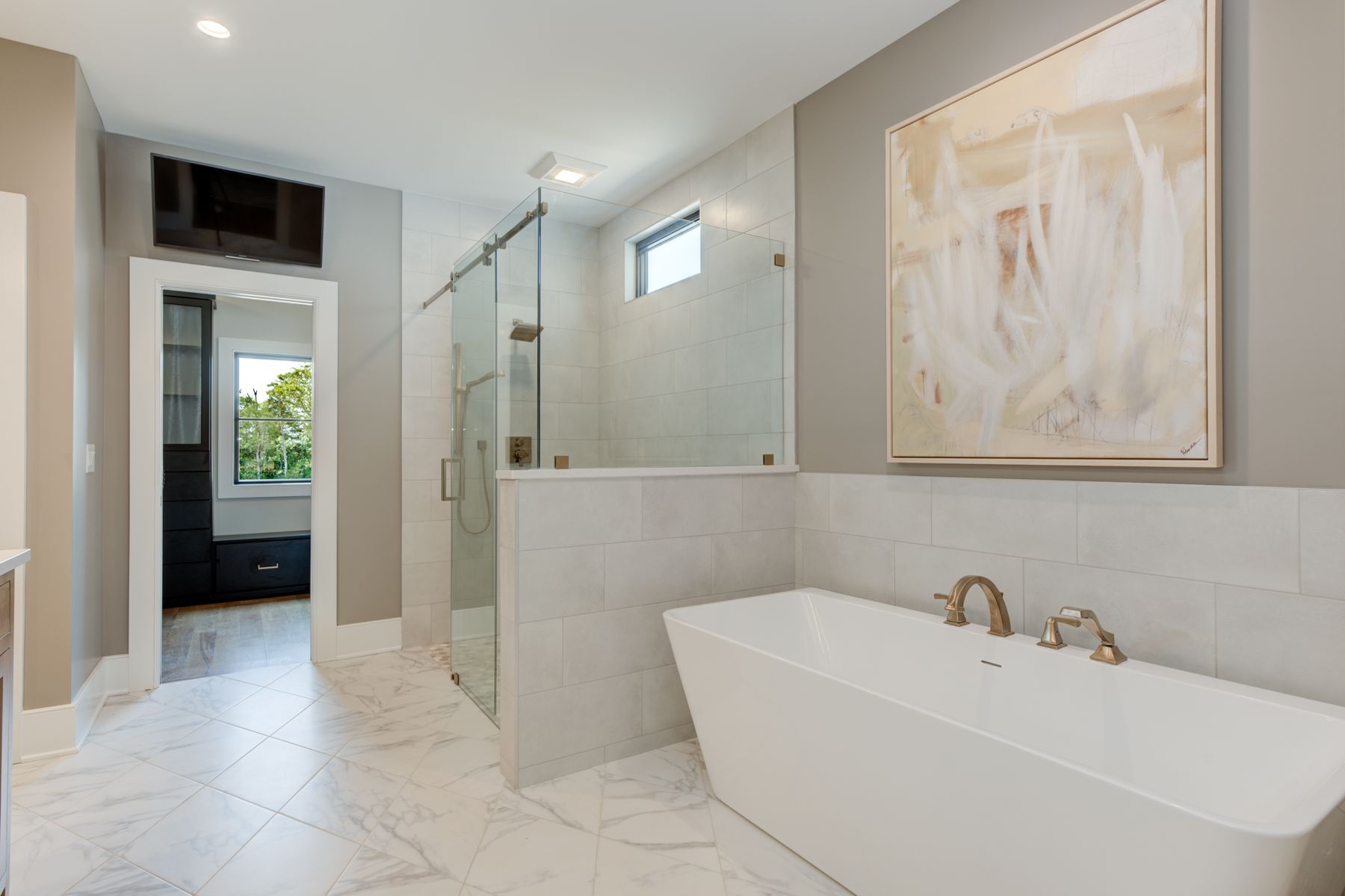 Modern bathroom with white tub, glass shower, and gray walls, a painting, and a small tv.