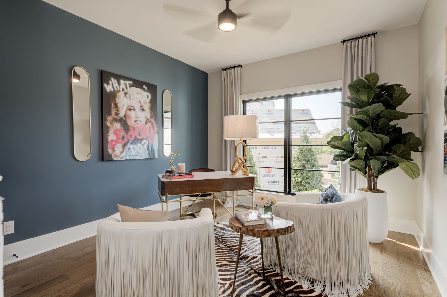 Office with blue accent wall, desk, fringed chairs, artwork, and large plant.