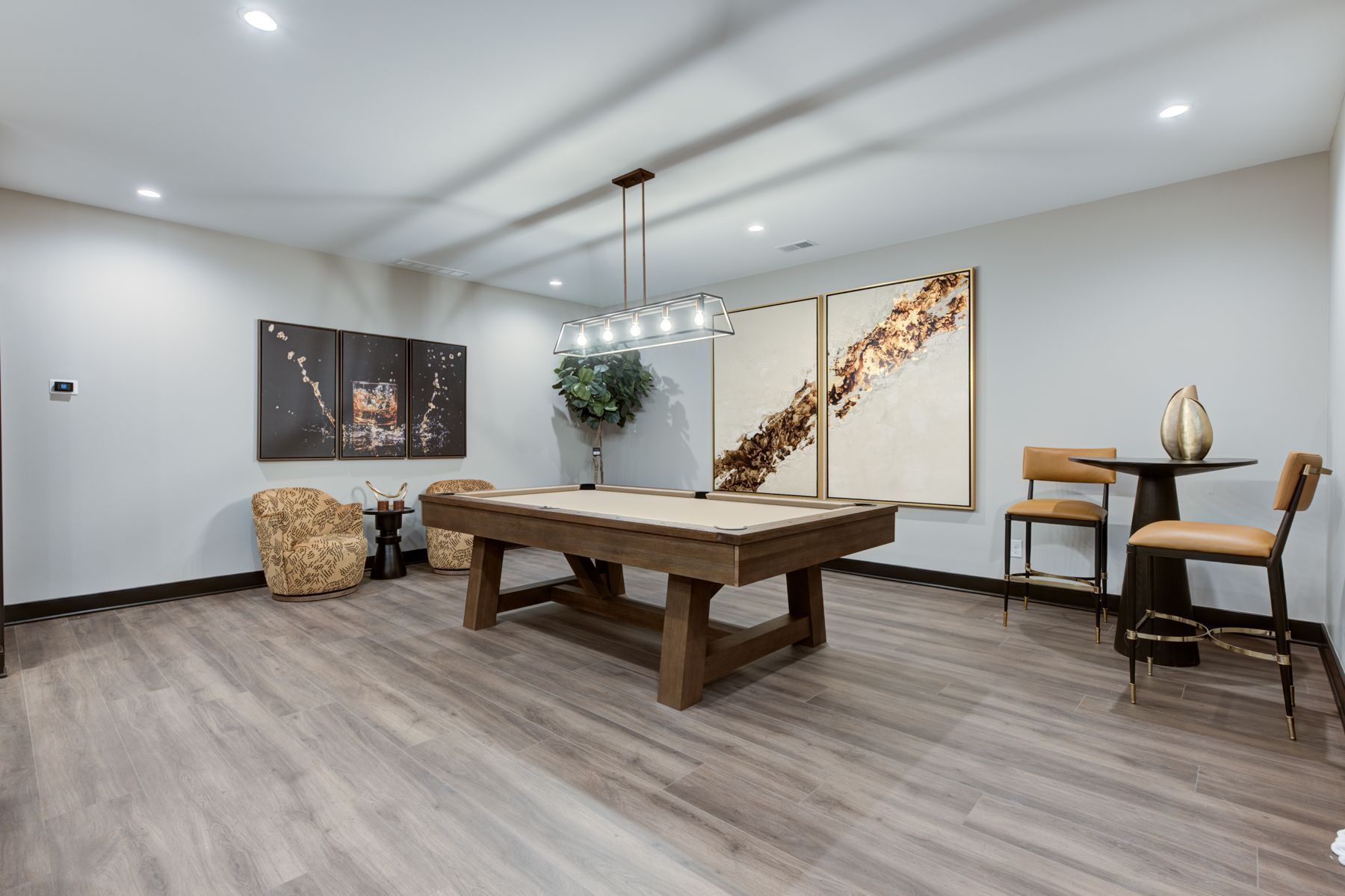 A recreation room with a pool table, artwork, bar stools, and hardwood flooring.