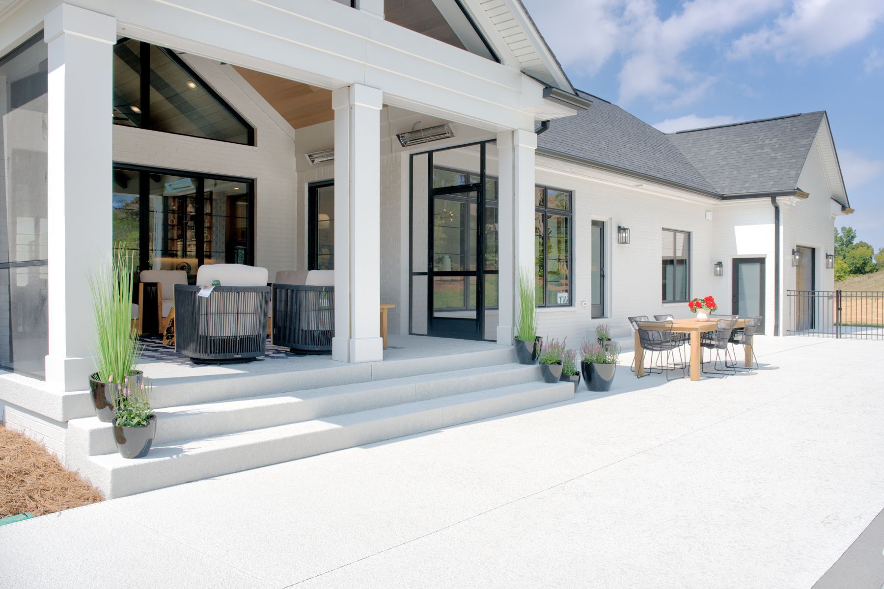White house exterior with patio, steps, seating, and dining table on a sunny day.