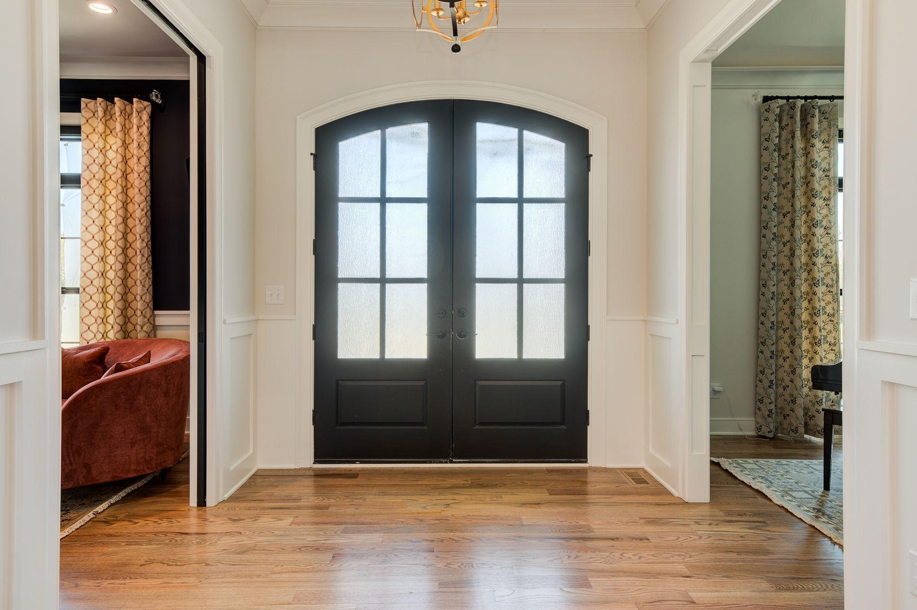 A hallway with wooden floors, black double doors with frosted glass, and white walls with open doorways to adjacent rooms.