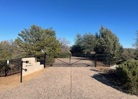 A metal gate is open to a driveway with trees in the background