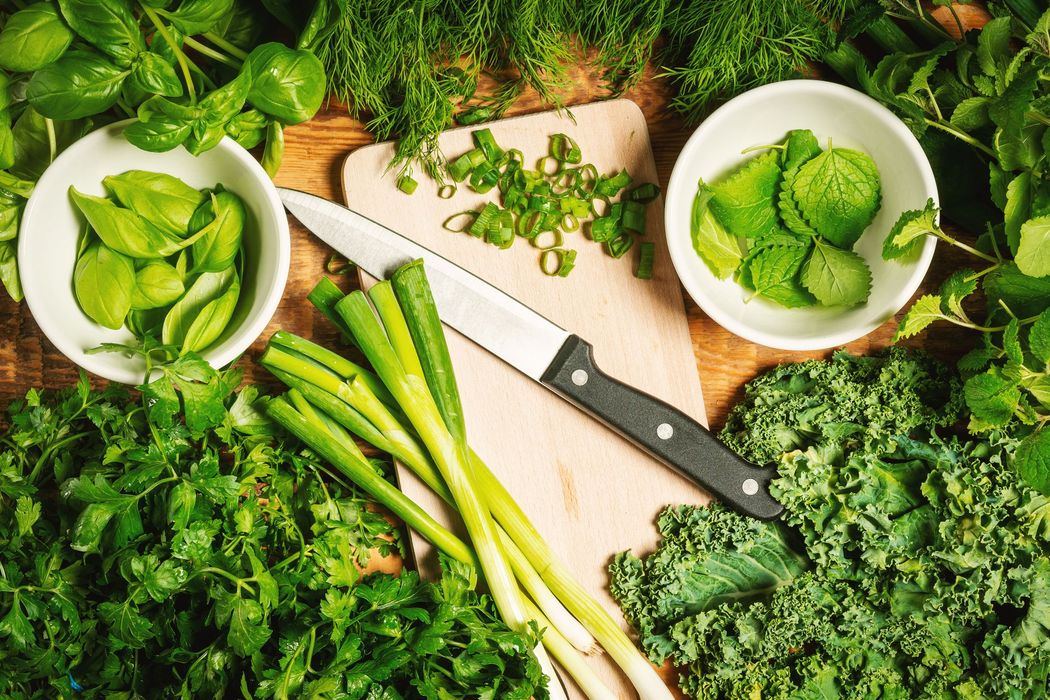 Verdure fresche e erbe aromatiche disposte su un tavolo rustico con due ciotole bianche e un coltello da cucina.