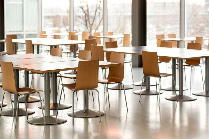 Caffetteria moderna e vuota con sedie in legno e tavoli rotondi, immersa in una luminosa luce naturale.