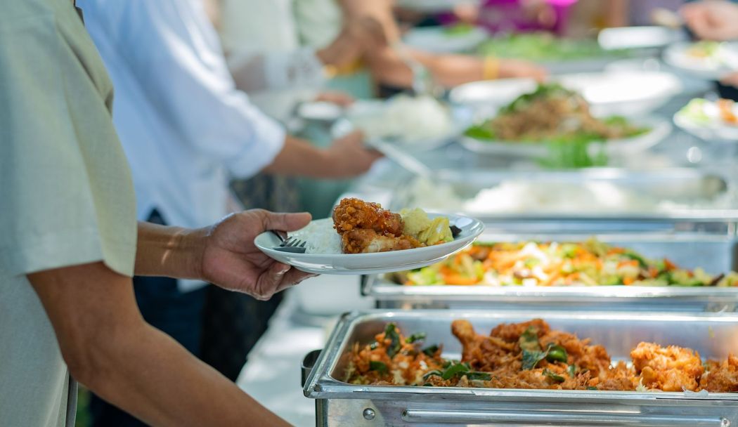 Persone che servono cibo a un buffet con vassoi di pietanze calde e piatti in mano