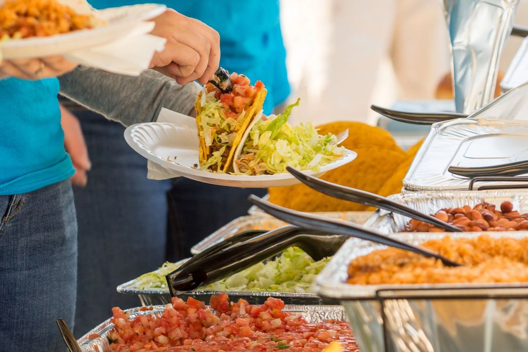 Persone che si servono da sole a un buffet con insalate, pasta e vassoi di cibo
