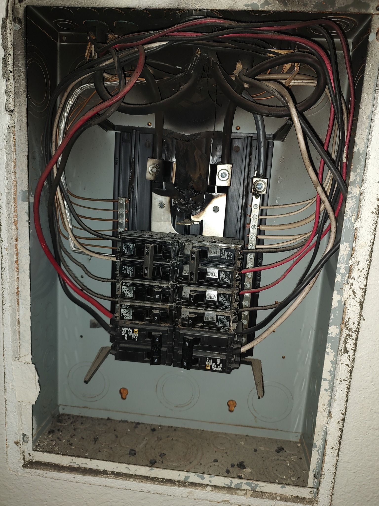 An open residential electrical breaker panel showing wires, metal components, and heavy charring from an electrical fire.