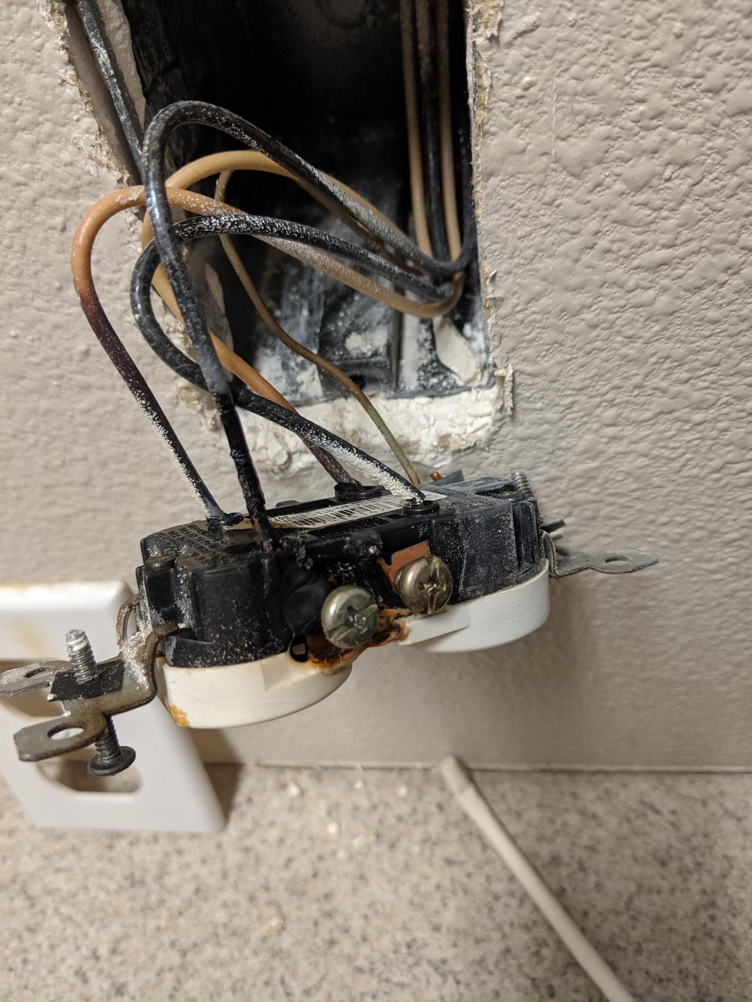 A wall outlet pulled from its housing, showing charred, damaged plastic and scorched electrical wires.
