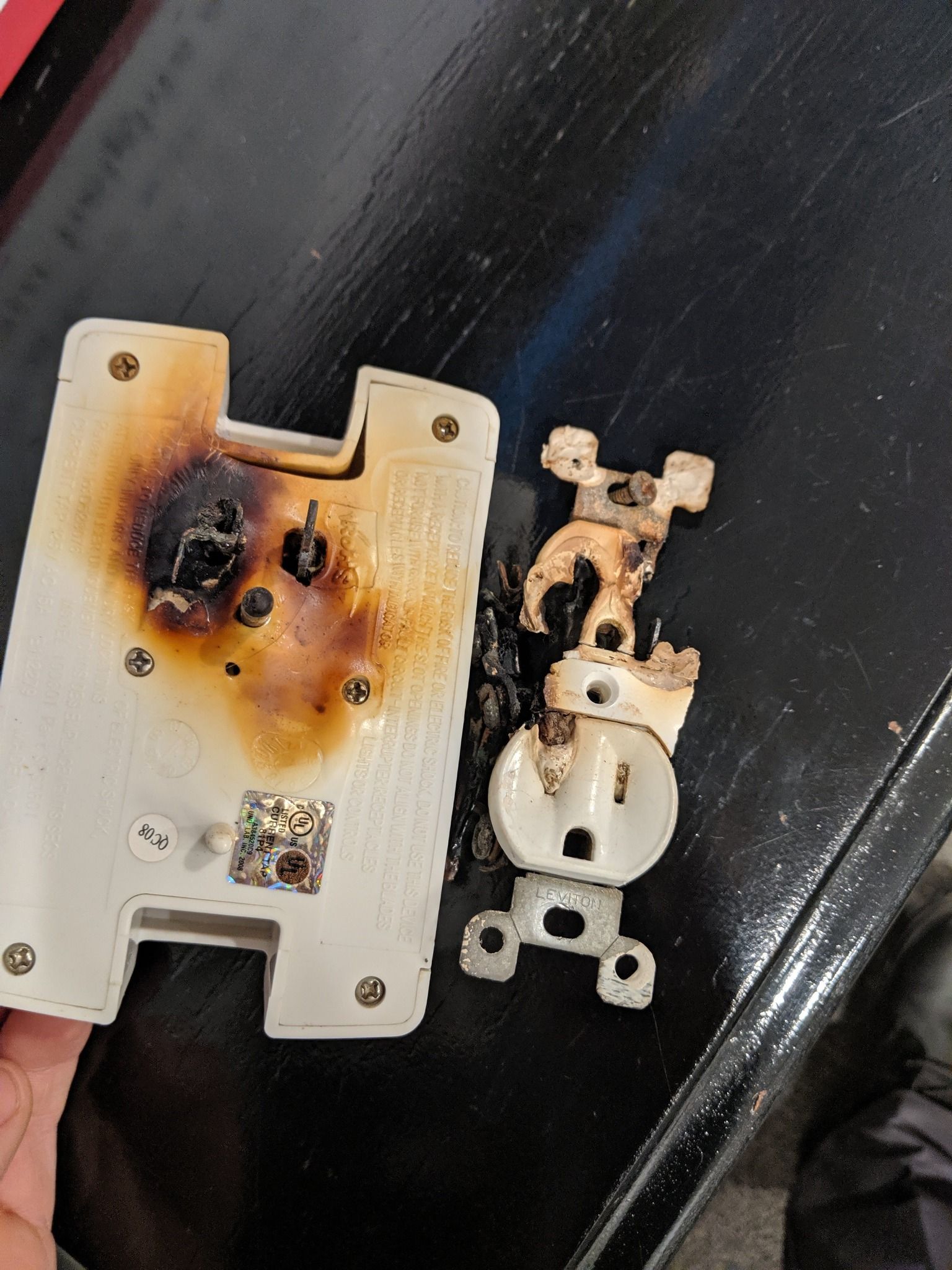 A damaged, charred white electrical outlet assembly, including the plastic wall plate and internal metal components.