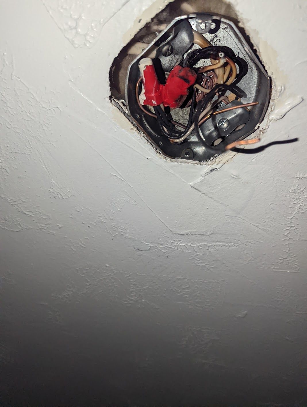 An open metal electrical box in a white ceiling with several wires connected by red plastic wire nuts.