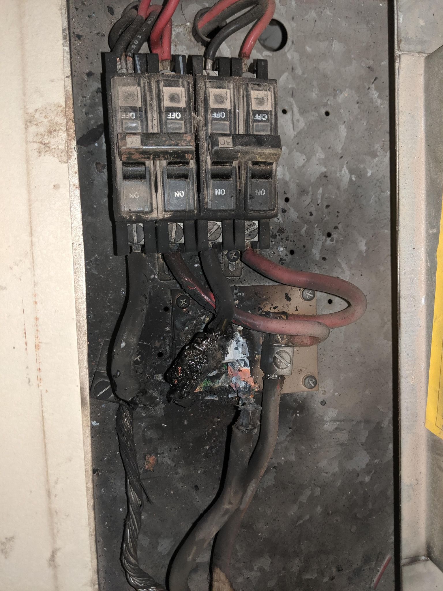 An electrical panel with melted and charred wiring, showing severe fire damage to the terminal block and surrounding area.