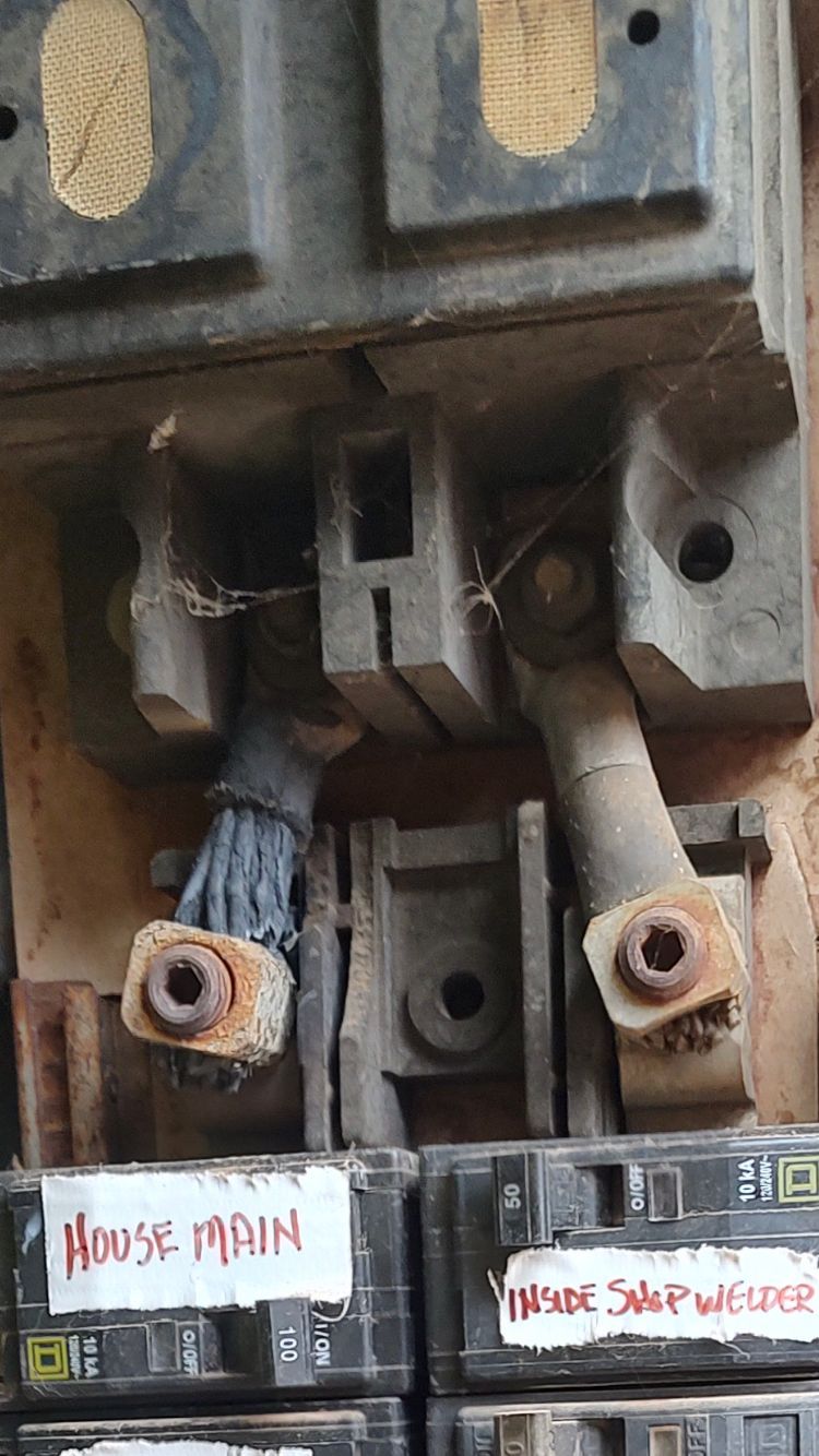 A close-up view of an open electrical breaker panel showing frayed wires connected to terminals above labeled switches.