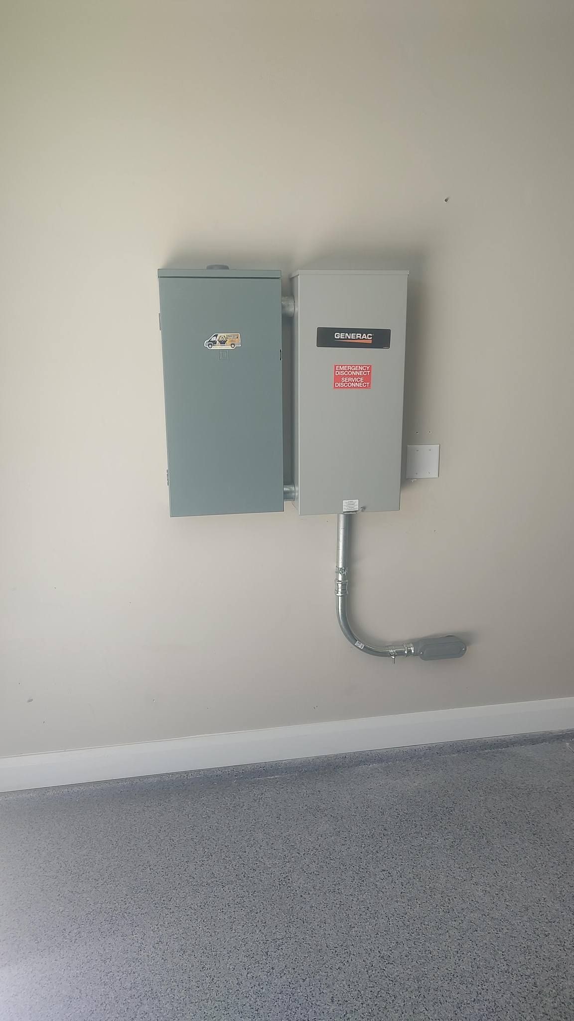 Two gray electrical service boxes mounted on a beige wall above a speckled epoxy garage floor.