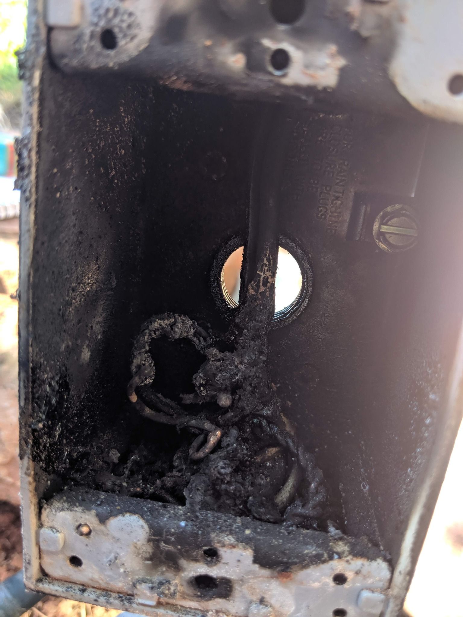 A metal electrical box containing wires severely damaged by fire, leaving the internal components charred and blackened.