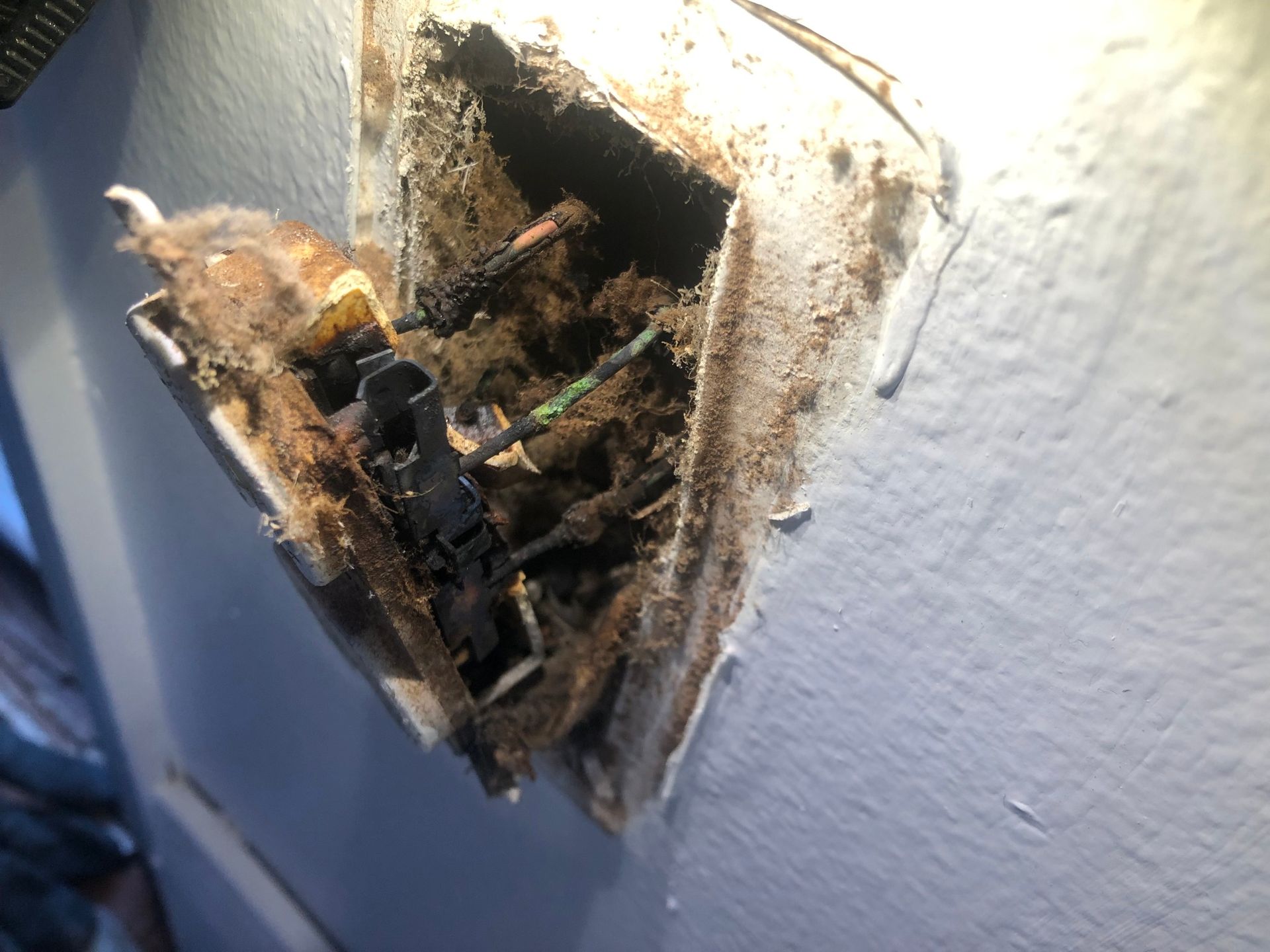 A damaged, charred electrical outlet pulled from a wall, showing exposed, blackened wires and debris inside the wall box.
