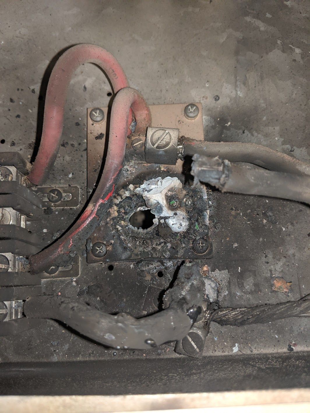 A severely charred and melted electrical terminal block with damaged wiring inside an electrical enclosure.