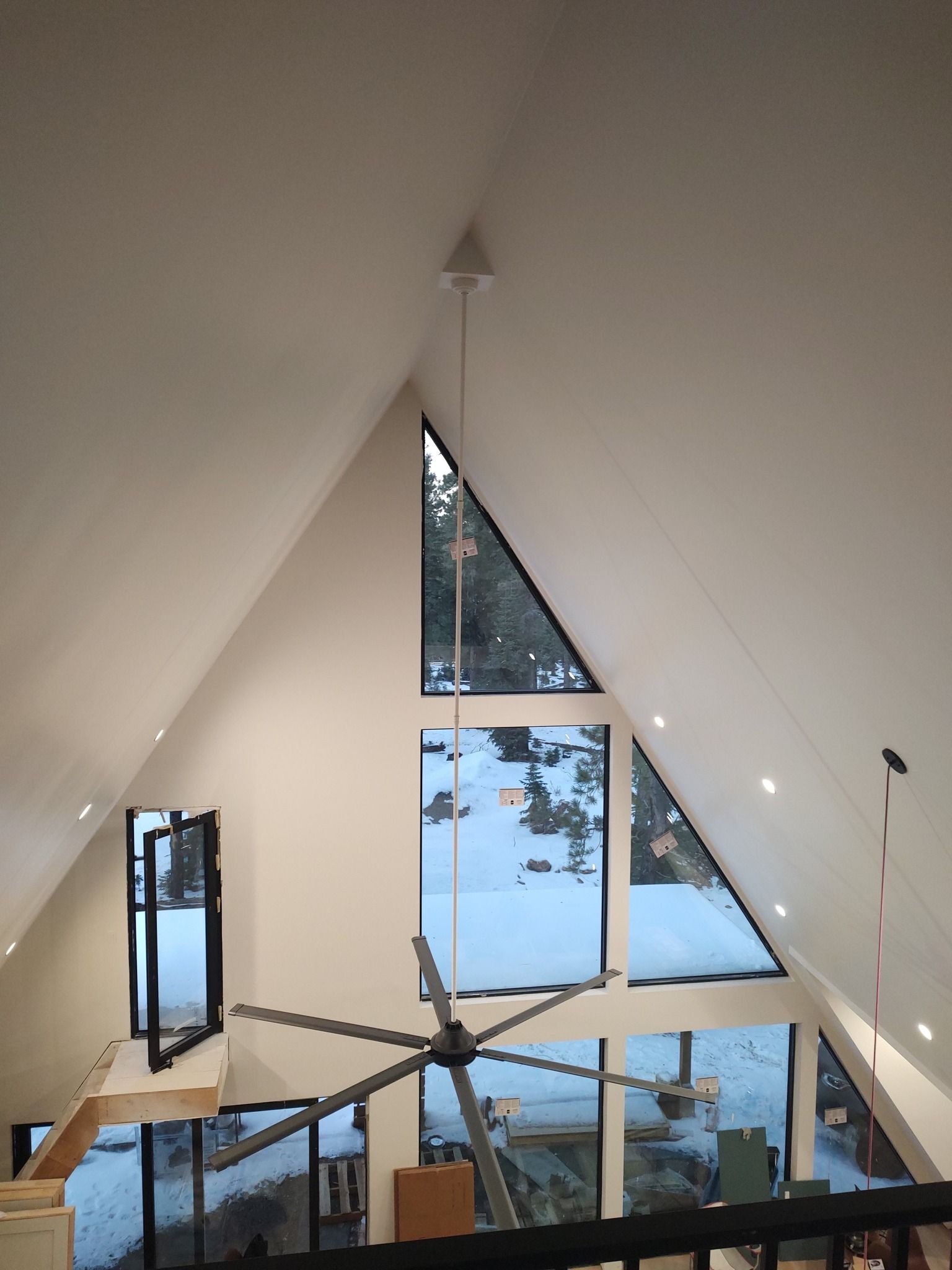 A tall, A-frame room with white walls, a large ceiling fan, and floor-to-ceiling windows looking out onto snowy terrain.