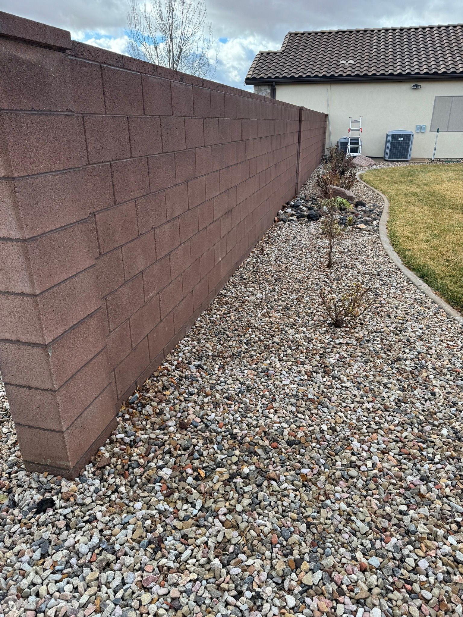 A red brick wall borders a gravel yard next to a house with a tiled roof.