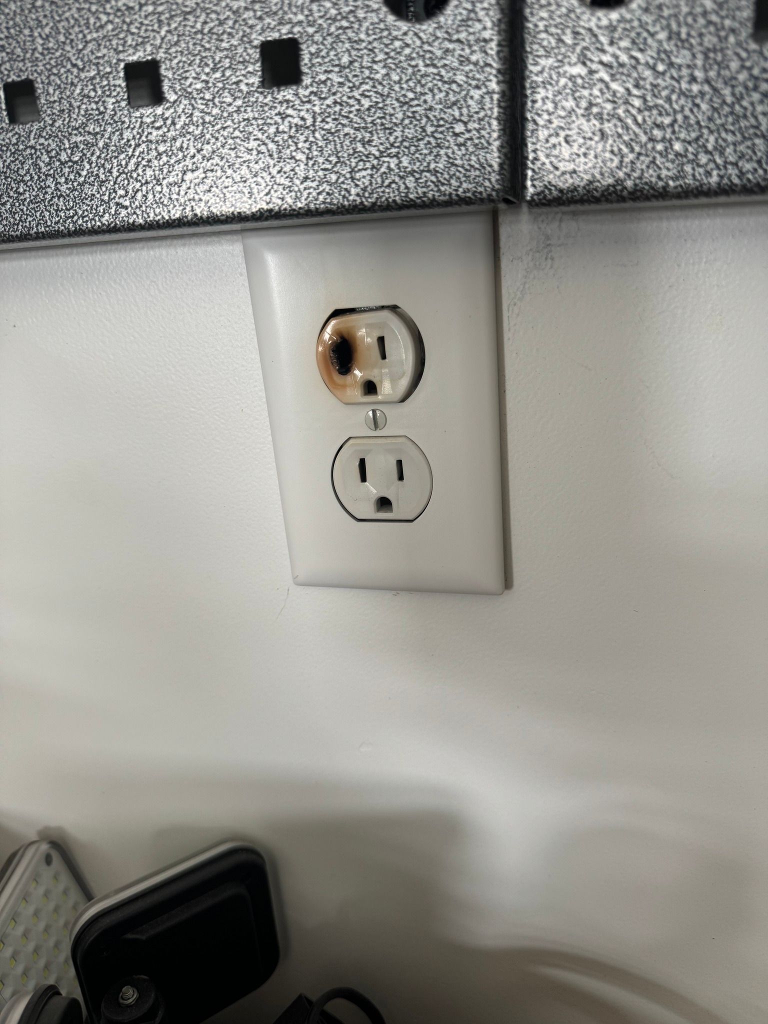 A white electrical wall outlet with a charred, burnt-looking burn mark on the top socket.