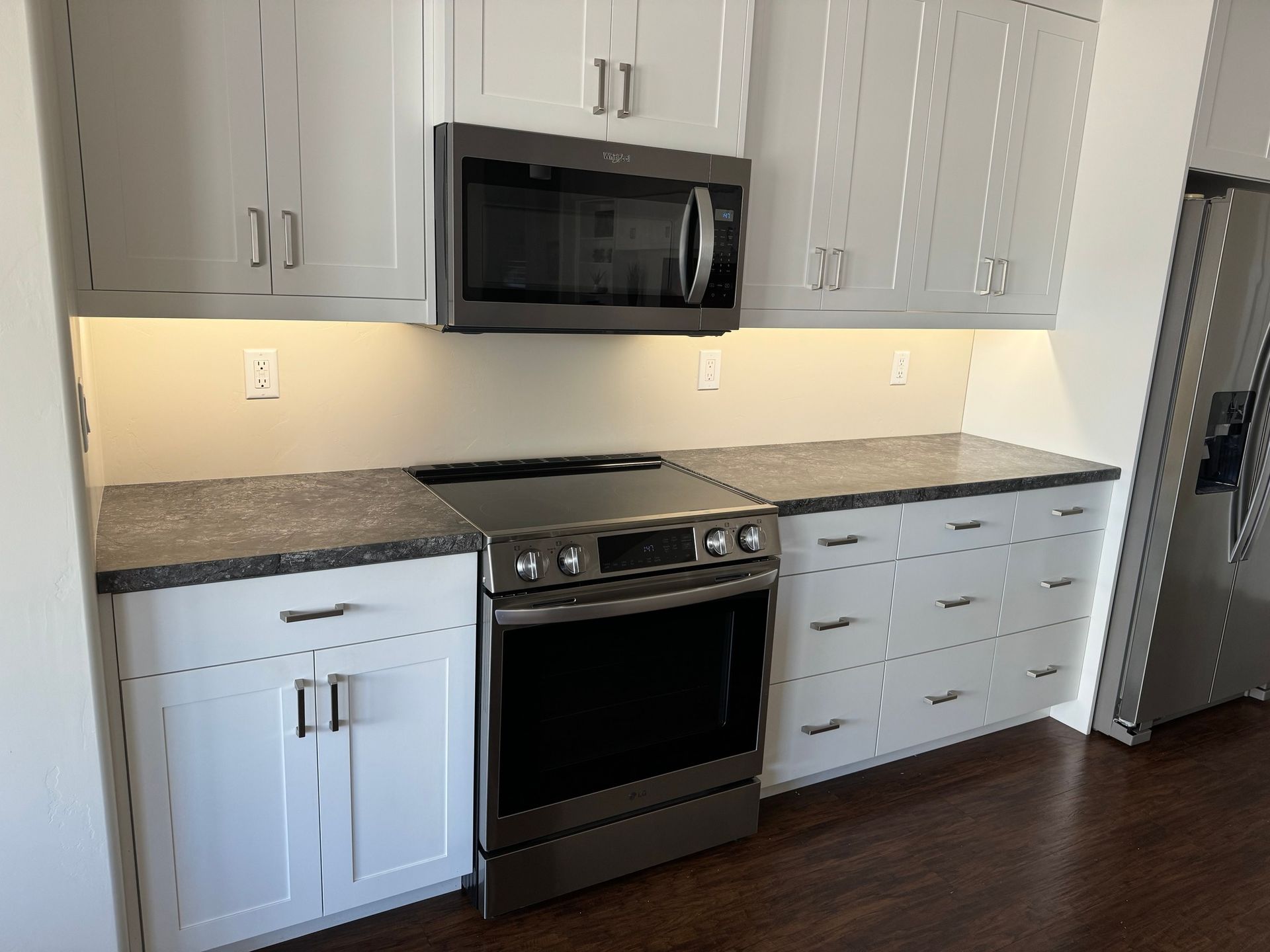 A modern kitchen featuring white cabinets, dark gray countertops, a stainless steel oven, and a built-in microwave.
