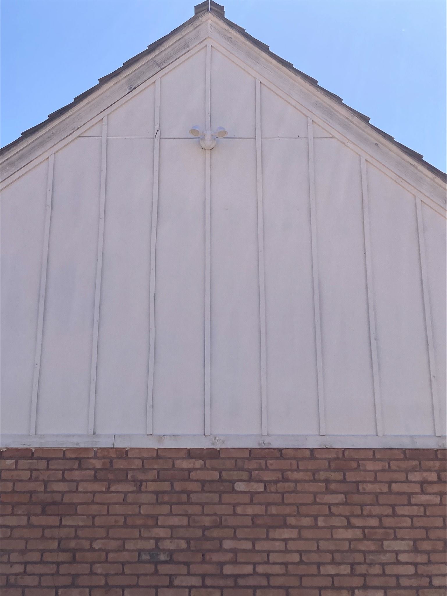 Gable end of a building with vertical white siding over a brick base, featuring a small sculpted animal head.