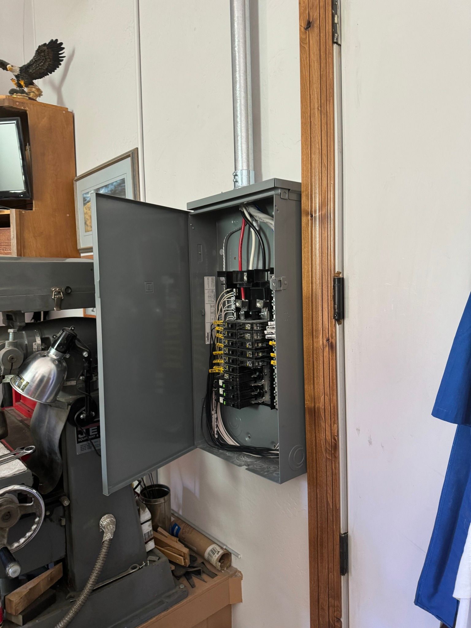 An open electrical breaker panel mounted on a white wall next to a large piece of industrial machinery.