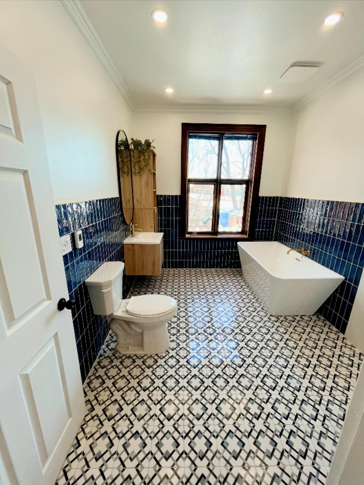 Salle de bains avec murs carrelés bleus, sol à motifs et équipements sanitaires blancs.