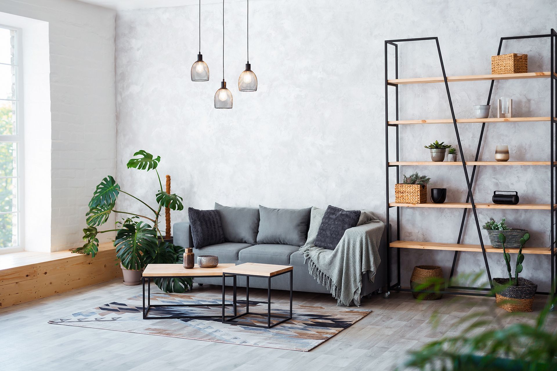 Salon avec canapé gris, étagères en bois, plantes et suspensions lumineuses.