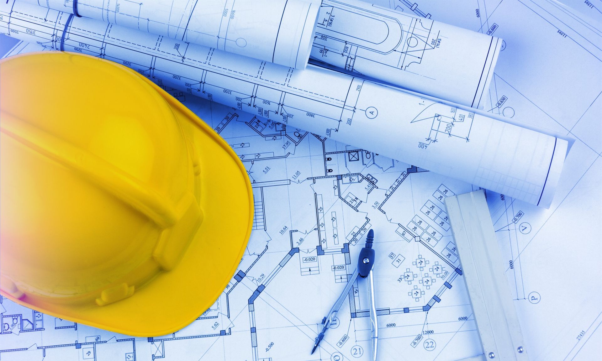 Casque jaune, plans roulés, compas de dessinateur et règle sur des plans architecturaux.