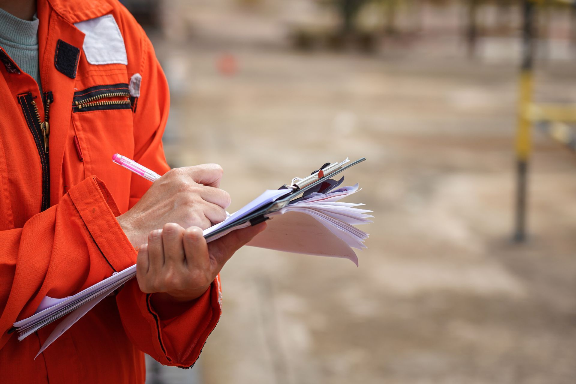 Un homme portant une veste orange tient un presse-papiers et écrit dessus.