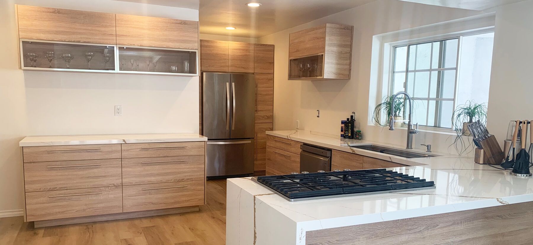 Modern kitchen with light wood cabinets, stainless steel appliances, and a white countertop island.