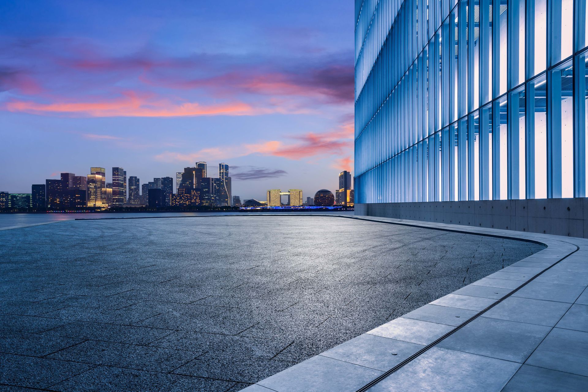 An empty street in front of a building with a city skyline in the background.