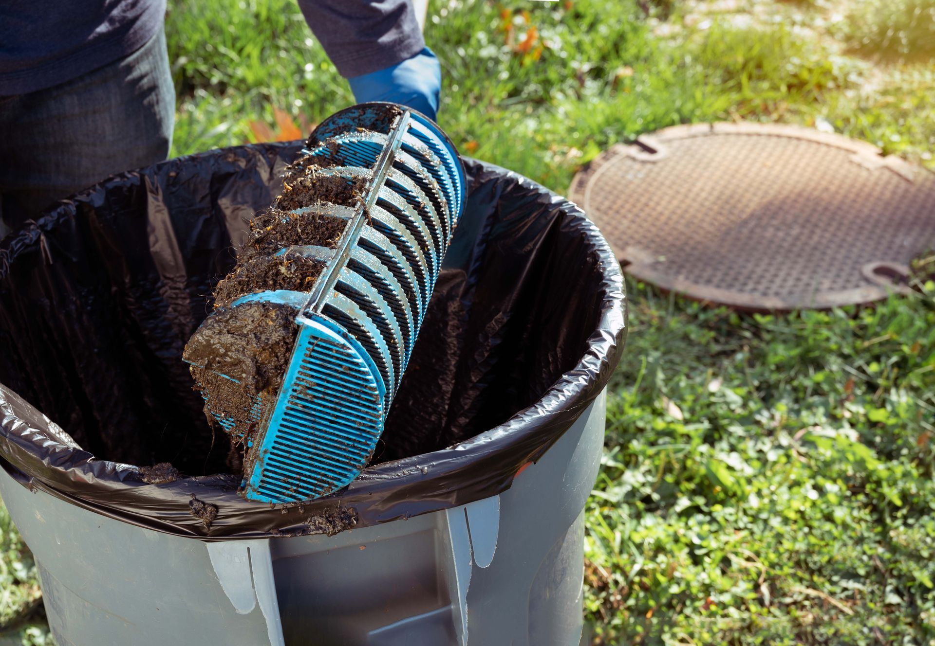 A person is cleaning a trash can with a blue scoop.