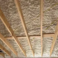 Spray foam insulation applied between wooden ceiling joists and rafters.