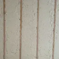 Insulated wall cavities showing white spray foam insulation between wooden wall studs.