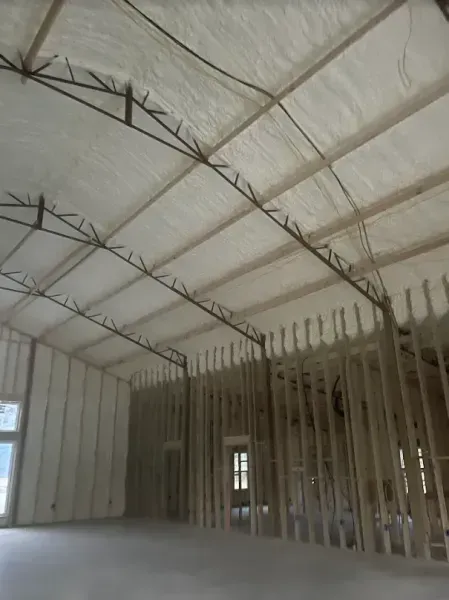 Interior view of a building under construction featuring exposed wood framing, metal trusses, and white spray-foam insulation.