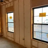 Interior view of a residential construction site showing two windows framed by bare wall studs and insulation.
