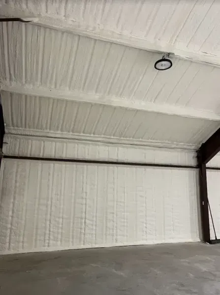 The interior of a storage building with white spray foam insulation covering the walls and arched ceiling.