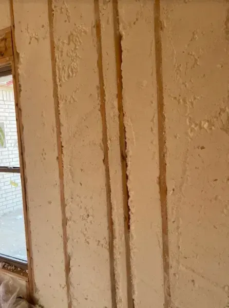 A wall with vertical wooden studs exposed between panels of textured, off-white insulation material.
