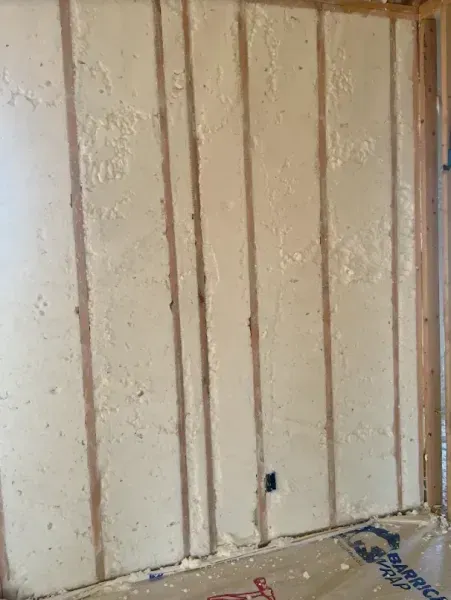 Spray foam insulation installed between wooden wall studs in an unfinished room.